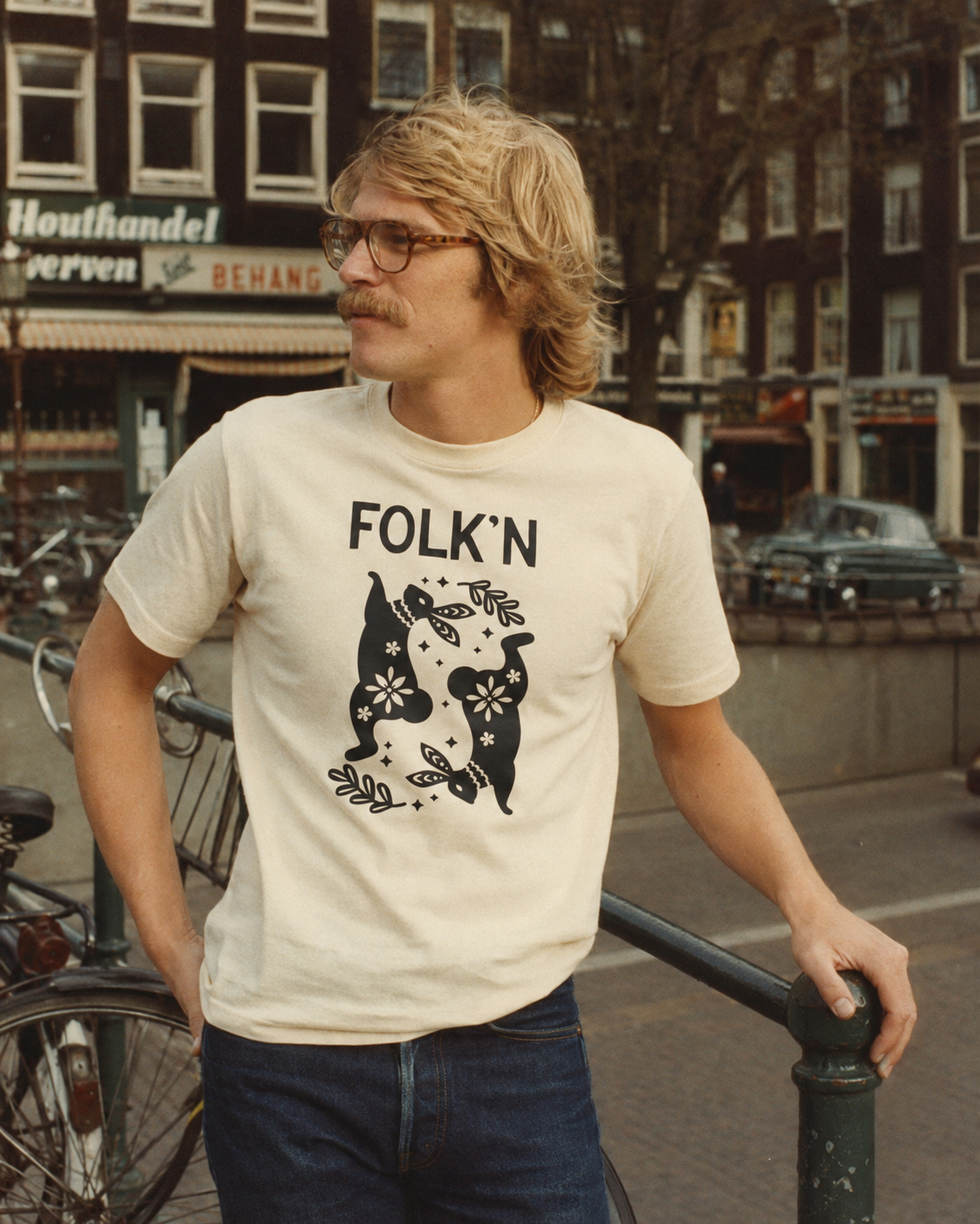 Folk'n dancing dogs tee — blonde man with mustache on a canal bridge.